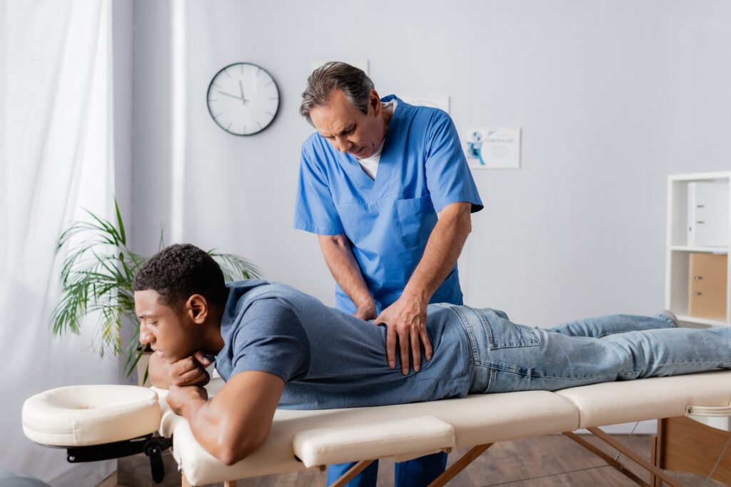 middle aged chiropractor working with injured back of african american patient on massage table in clinic