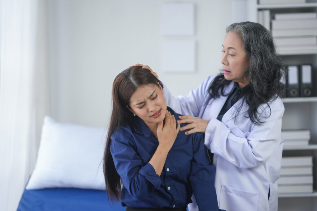 Doctor examining a patient's neck pain in a medical office. The patient appears to be in discomfort while receiving professional care.